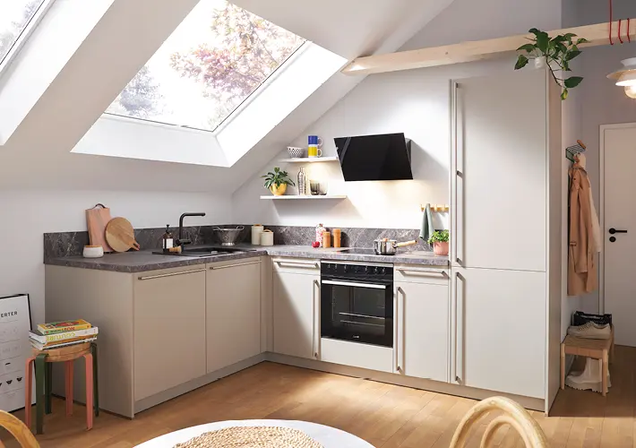 Helle Eckküche unter Dachschräge mit großem Dachfenster, Backofen, Spüle und dunkler Arbeitsplatte auf Holzboden.